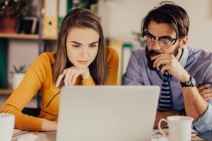 Junge Frau und Mann blicken konzentriert auf aufgeklappten Laptop