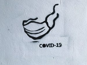 Arbeitsrecht und Corona - Graffiti mit Maske an weißer Wand